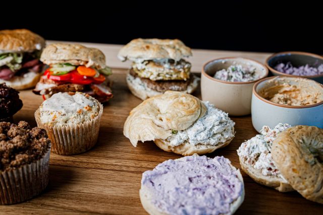 Selection of bagels, muffins, and smears arranged on a large wooden cutting board.